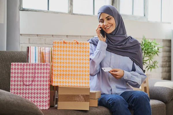 Młoda arabka trzymająca wizytówkę, rozmawiająca przez telefon i patrząca na prezenty Obraz Stockowy