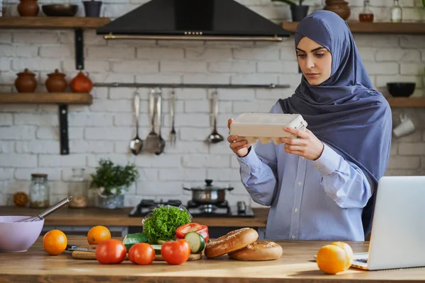 Mujer árabe joven sosteniendo una bandeja con huevos y leyendo atentamente la etiqueta —  Fotos de Stock