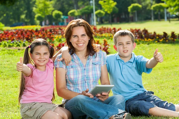 Familia feliz usando el ordenador portátil acostado en la hierba —  Fotos de Stock