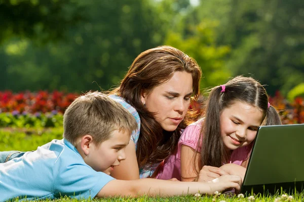 Glückliche Familie mit Laptop im Gras liegend — Stockfoto