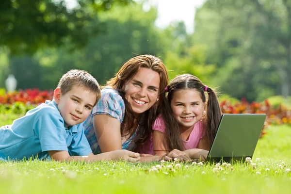 Familia feliz usando el ordenador portátil acostado en la hierba — Foto de Stock