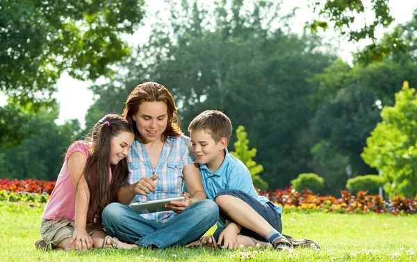 Familia feliz usando el ordenador portátil acostado en la hierba — Foto de Stock