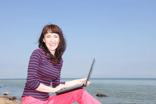 A woman on a sunny beach working on a laptop — Stock Photo, Image