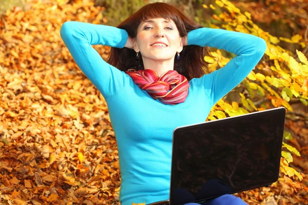 Donna sorridente con laptop nel parco autunnale — Foto Stock