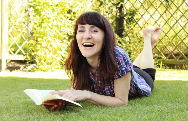 Smiling woman reading book on the grass in garden — Stock Photo, Image