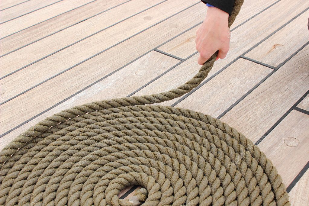 Hand of woman and thick rope wrapped in spiral lying on deck of