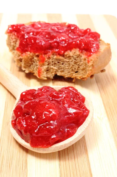 Strawberry jam on wooden spoon and whole wheat bread — Stock Photo, Image