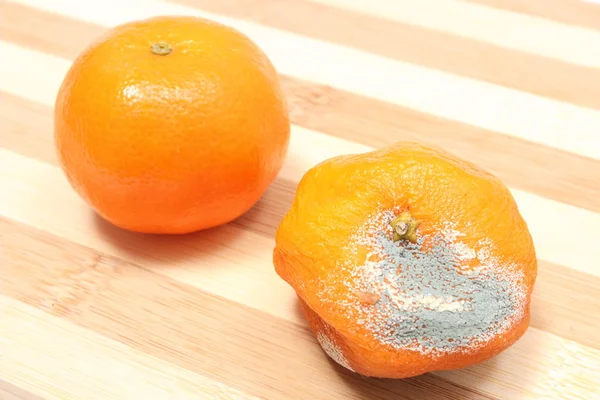 Fresh and moldy mandarins on wooden background — Stock Photo, Image