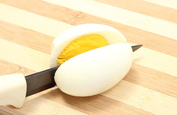 Closeup of knife cutting egg on wooden background — Stock Photo, Image