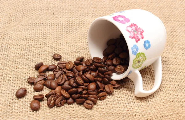 Heap of coffee grains with overturned cup — Stock Photo, Image