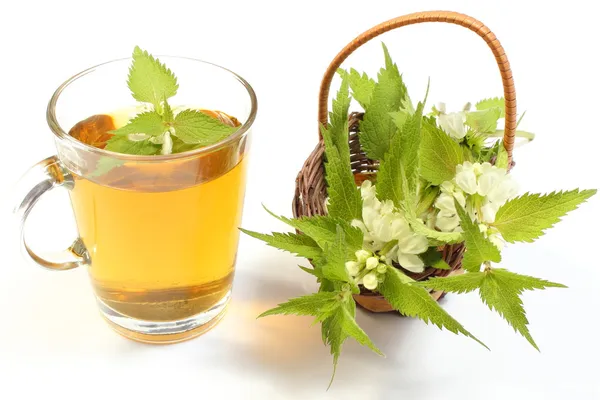 Fresh nettle in wicker basket and cup of beverage — Stock Photo, Image