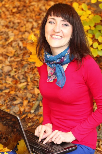 Smiling woman with laptop in autumn park — Stock Photo, Image