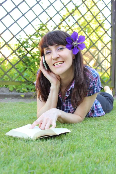 Lächelnde Frau mit Buch und Handy im sonnigen Garten — Stockfoto