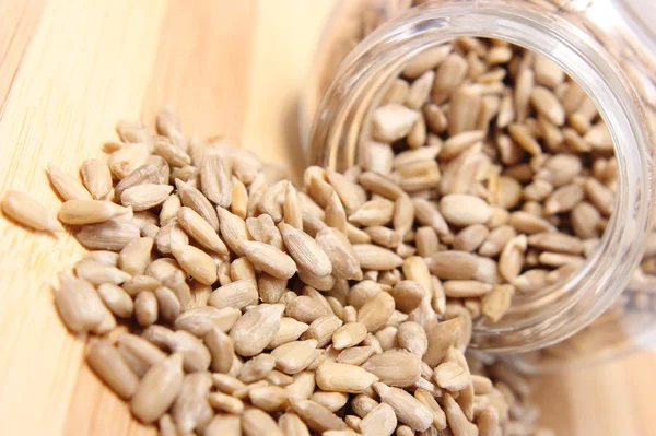 Heap of sunflower seeds in glass jar on wooden cutting board — Stock Photo, Image