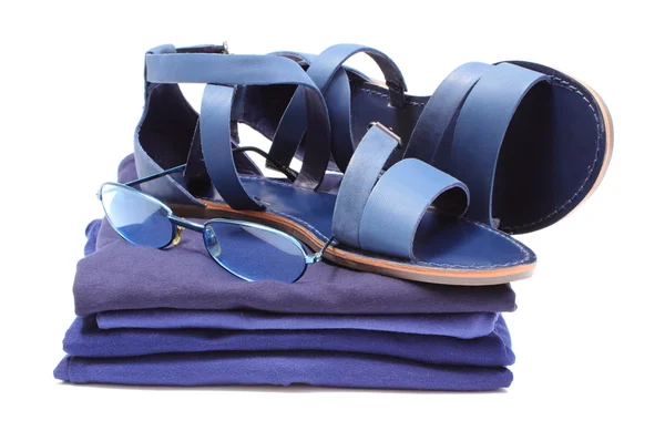 Womanly sandals and sunglasses on pile of blue clothes. White background — Stock Photo, Image