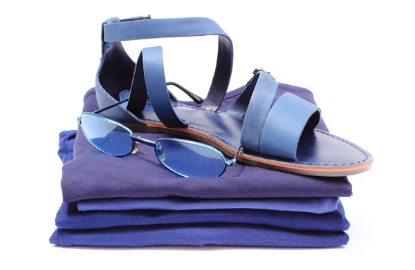Жіночі сандалі та сонцезахисні окуляри на купі синього одягу. Білий фон — стокове фото