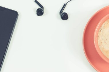 Kulaklıklı akıllı telefon ve sütlü kahve. Müzikle rahatlama zamanı. Beyaz arka plan. Metin veya yazı için yer