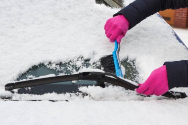 Araba ve ön camlardan kar temizleyen bir kadın eli. Ulaşım sırasında kış sorunları