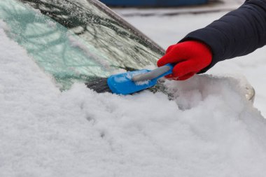 Araba ve ön camlardan kar temizleyen bir kadın eli. Ulaşım sırasında kış sorunları