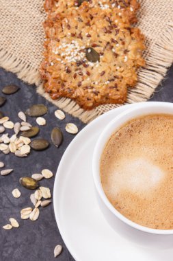 Bir fincan kahve ve ballı ev yapımı yulaflı kurabiye ve farklı sağlıklı tohumlar. Lezzetli çıtır tatlı.