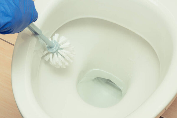 Hand of cleaner using brush for cleaning toilet in bathroom. Household duties concept