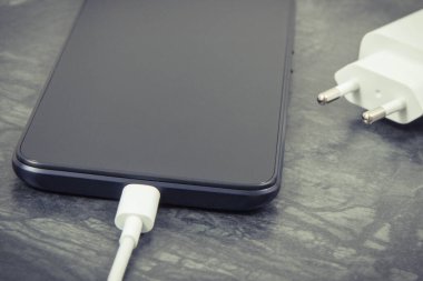 Şarj cihazına bağlı siyah bir cep telefonu. Akıllı telefon şarj ediliyor