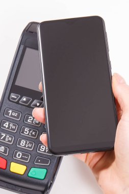 Nakitsiz ödeme yapmak için akıllı telefon ve ödeme terminalini kullanan bir kadın eli. Finans ve bankacılık kavramı