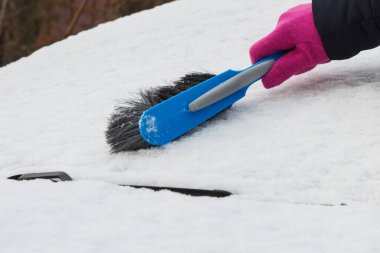 Araba ve ön camlardan kar temizleyen bir kadın eli. Ulaşım sırasında kış sorunları
