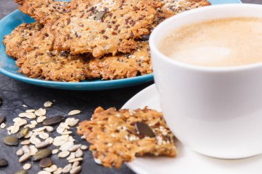 Bir fincan kahve ve ballı taze ev yapımı yulaf ezmesi kurabiyeleri ve farklı sağlıklı tohumlar. Lezzetli çıtır tatlı.