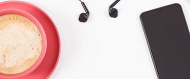 Cep telefonu bağlı kulaklıklar ve sütlü bir fincan kahve. Müzikle rahatlama zamanı. Beyaz arka plan. Metin veya yazı için yer