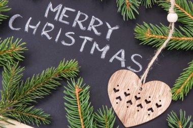 Yazılı Mutlu Noeller, yeşil ladin dalları ve siyah arka planda ahşap kalp şeklinde. Noel zamanı için dekorasyon