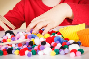 Anaokulu öğrencisi küçük pompodlar ve ahşap maşayla oynuyor. Çocukların motor becerilerinin, koordinasyonun, yaratıcılığın ve mantıksal düşüncenin geliştirilmesi