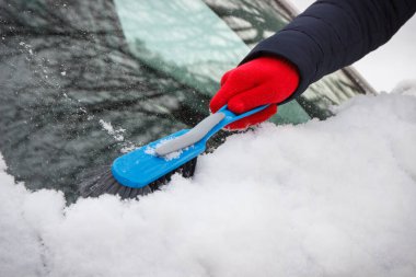 El fırçasıyla araba ve ön camdan kar temizliyor. Ulaşım sırasında kış sorunları