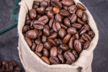 Koyu kavrulmuş kahve çekirdeği yığını beton yapıda jüt torba içinde.