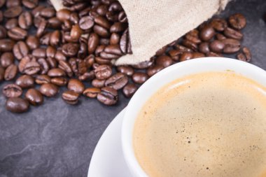 Beyaz cam bardakta kahve ve kavrulmuş kahve çekirdekleri.