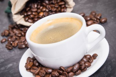 Beyaz cam bardakta kahve ve kavrulmuş kahve çekirdekleri.