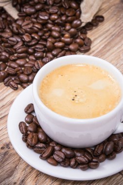 Beyaz cam bardakta kahve ve kavrulmuş kahve çekirdekleri.