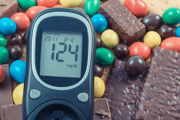 Glucose meter for checking sugar level and heap of sweets containing a lot of sugar. Unhealthy and caloric eating