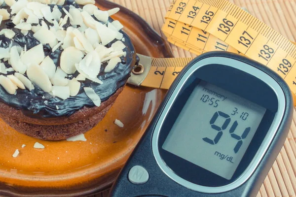 Glucometer with result of measurement sugar level, fresh baked chocolate muffins and tape measure. Diabetes, slimming and dessert for different occasions