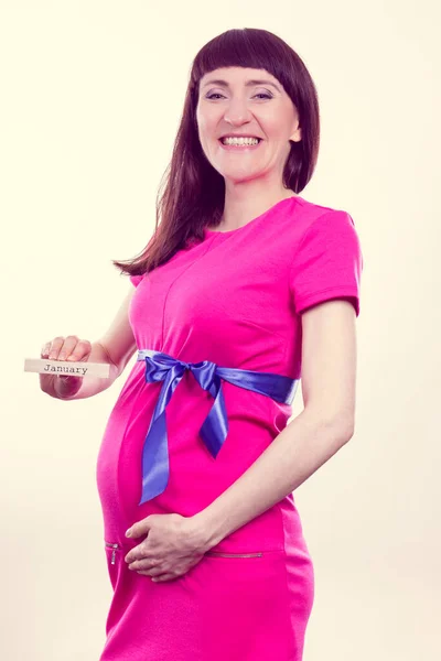 木製のキューブに書かれた単語1月を示す青いリボンとピンクのドレスの幸せな笑顔妊婦 新生児や家族の拡大への期待 — ストック写真