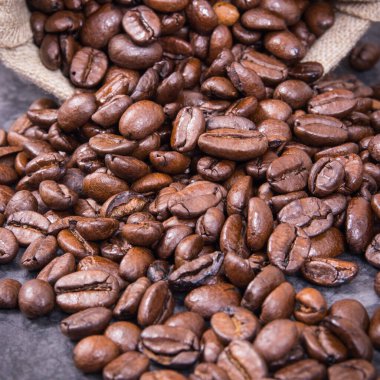 Koyu kavrulmuş kahve çekirdeği yığını beton yapıda jüt torba içinde.