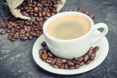 Beyaz cam kahve fincanı ve kavrulmuş koyu kokulu kahve taneleri.