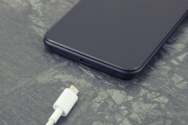 Siyah cep telefonu ve bağlanmamış şarj kablosu. Akıllı telefon şarj oluyor. Siyah arkaplan