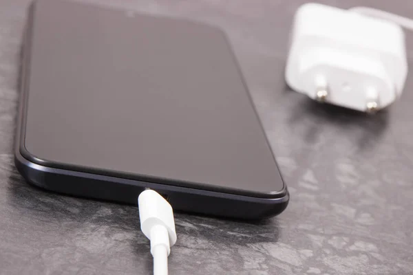 Black smartphone and unconnected cable of charger. Mobile phone charging