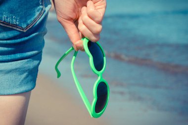 Plajda kalp şeklinde güneş gözlüklü bir kadın eli. Yaz ve tatil zamanı