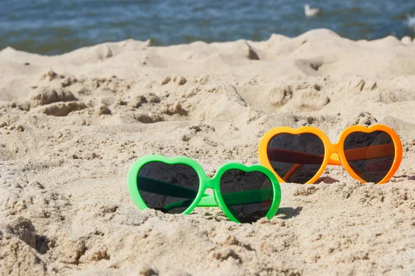 Kumsalda kumsalda renkli güneş gözlükleri. Güneş banyosu sırasında güneş koruması. Seyahat ve tatil zamanı kavramı