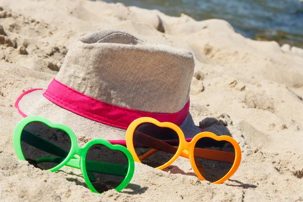 ビーチで砂の上にカラフルなサングラスや麦藁帽子 日光浴中の太陽の保護 旅行と休暇の時間の概念 — ストック写真