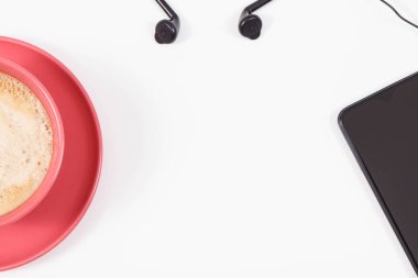 Cep telefonu bağlı kulaklıklar ve sütlü bir fincan kahve. Müzikle rahatlama zamanı. Beyaz arka plan. Metin veya yazı için yer