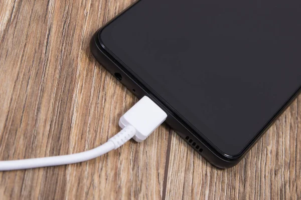 Black smartphone and connected white cable of charger. Mobile phone charging