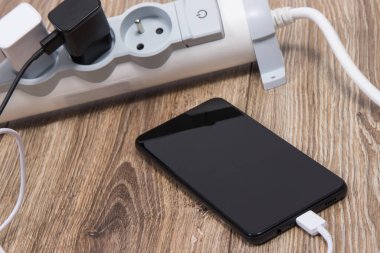 Siyah akıllı telefon, cep telefonu ve elektrik hattına bağlı şarj cihazları. Çeşitli aygıtlar şarj etme kavramı